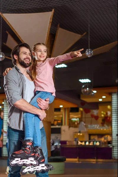 Улыбающийся отец держит дочь в роликовых коньках на катке — стоковое фото