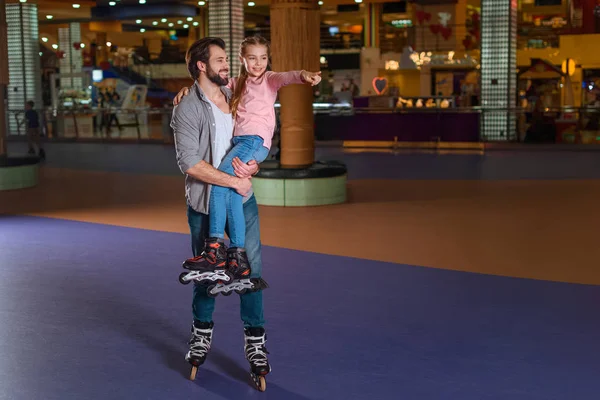 Pai feliz segurando filha em patins no rinque de rolo — Fotografia de Stock