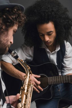 young duet of musicians playing sax and acoustic guitar on black clipart