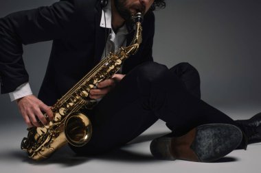 cropped shot of musician playing saxophone while sitting on floor clipart