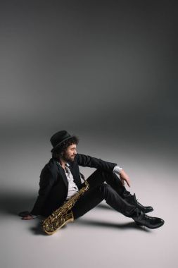 handsome musician sitting on floor with saxophone clipart