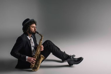 handsome jazzman playing saxophone while sitting on floor clipart