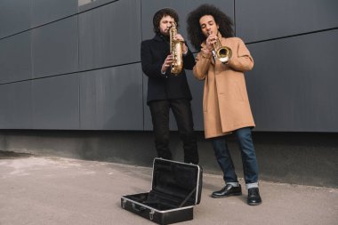 duet of street musicians playing trumpet and saxophone outdoors clipart