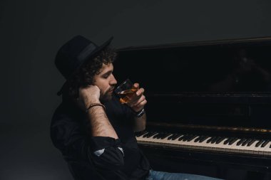 handsome musician drinking whiskey near piano on black clipart