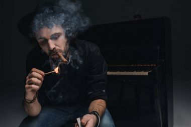 handsome bearded musician smoking cigar in front of piano on black clipart