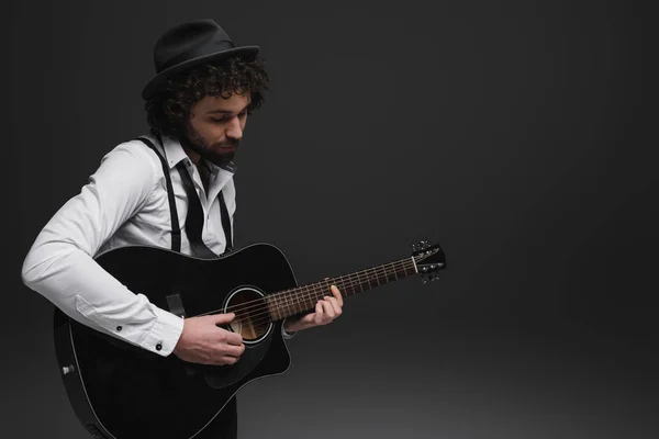 Красивый бородатый музыкант играет на акустической гитаре на черном — стоковое фото