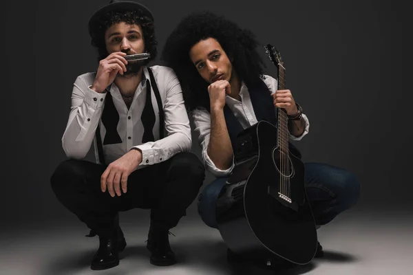 Duet of musicians with guitar and harmonica sitting squat — Stock Photo, Image