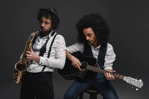 Duet of musicians playing sax and acoustic guitar on black — Stock Photo, Image