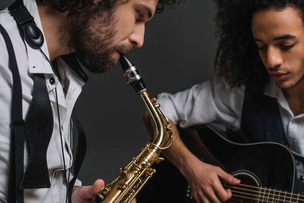 duet of jazzmen playing sax and acoustic guitar on black