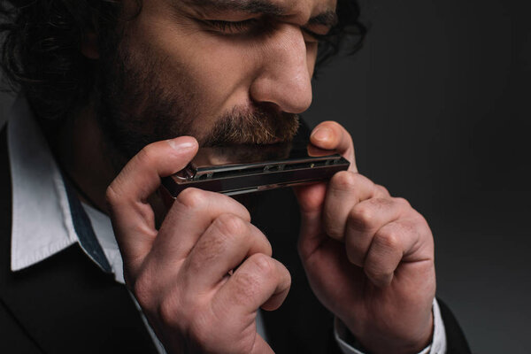 close-up portrait of expressive musician playing harmonica on black