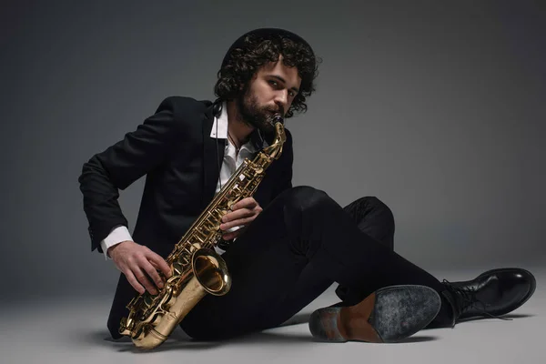 Bearded jazzman playing saxophone while sitting on floor — Stock Photo, Image