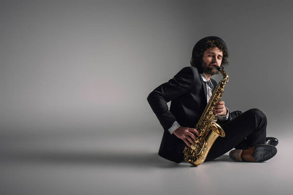 stylish musician playing saxophone while sitting on floor