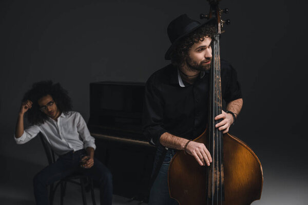 man playing violoncello while his depressed partner sitting at piano blurred on background