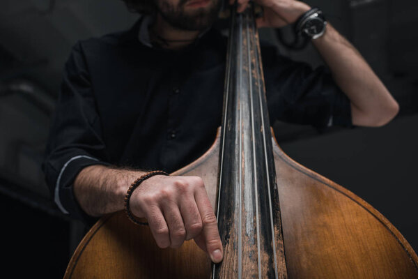 cropped shot of man playing double bass on black