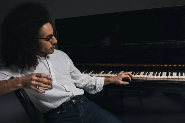 Guapo joven músico bebiendo whisky y tocando el piano en negro — Foto de Stock