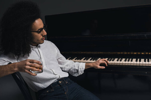 handsome young musician drinking whiskey and playing piano on black