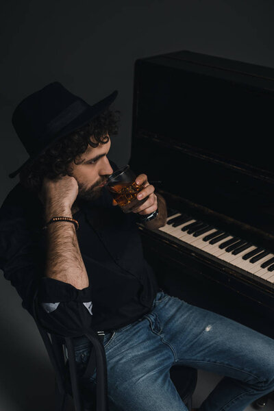 man with glass of whiskey sitting near piano on black