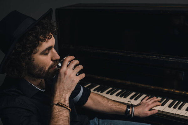 handsome musician drinking whiskey and playing piano