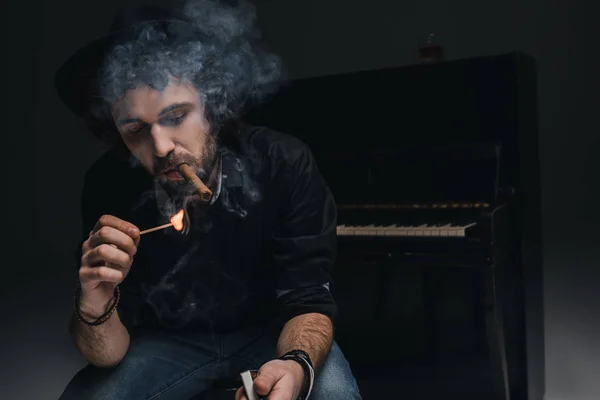 Handsome bearded musician smoking cigar in front of piano on black — Stock Photo, Image