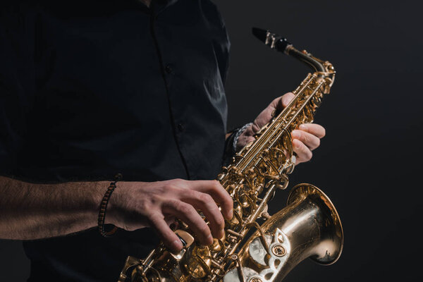 обрезанный снимок человека, играющего на саксофоне на черном
