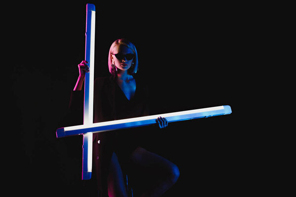 стильная модная девушка позирует с двумя ультрафиолетовыми лампами для моды съемки, изолированные на черном
