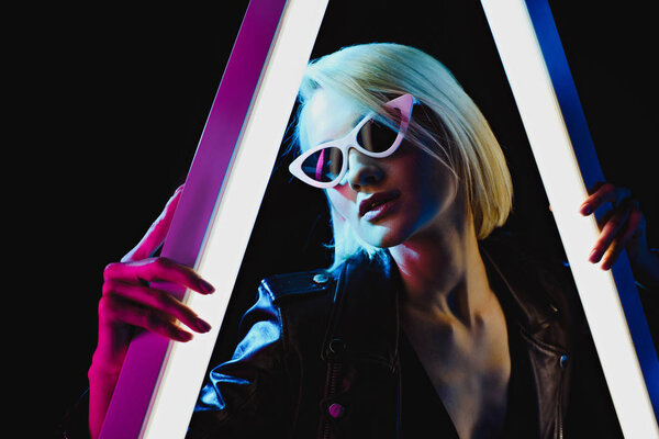 привлекательная модная девушка позирует в солнечных очках с двумя ультрафиолетовыми лампами, изолированными на черном

