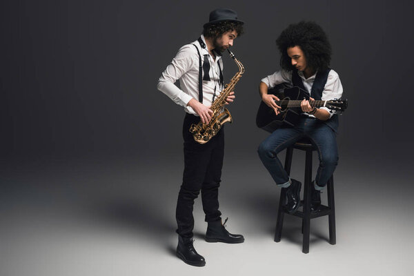 Stylish duet of musicians playing sax and acoustic guitar on black Stock Photo