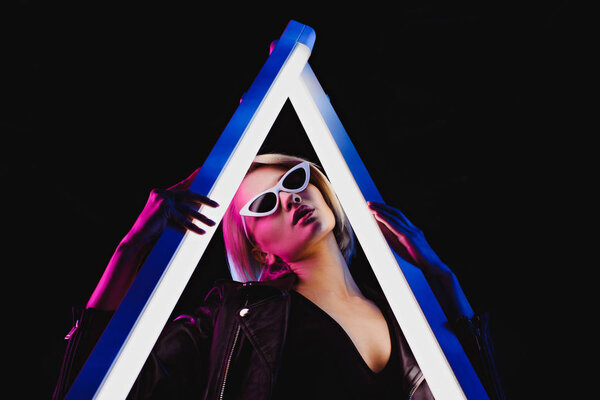 фешенебельная девушка позирует с двумя ультрафиолетовыми лампами для модной съемки, изолированная на черном
