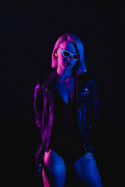 fashionable girl posing in black leather jacket and sunglasses, isolated on black