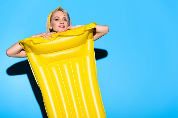 beautiful happy girl posing with yellow inflatable mattress on blue