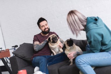 happy tattooed couple with dogs on sofa at home clipart