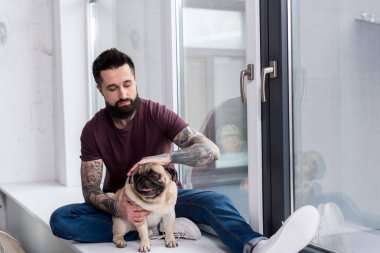 pencere kenarında oturan ve evde köpek palming dövmeli yakışıklı adam
