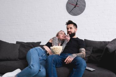 dövmeli çift evde kanepenin üzerinde patlamış mısır yemek