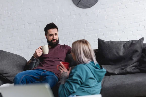 tattooed couple drinking coffee and looking at each other at home