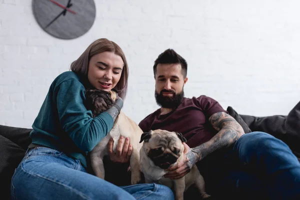 tattooed girlfriend hugging pug dog on sofa at home