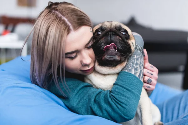 beautiful tattooed girl hugging funny pug at home