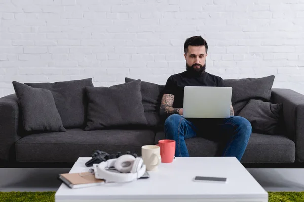 Tatuado Bonito Homem Usando Laptop Sofá Casa — Fotografia de Stock