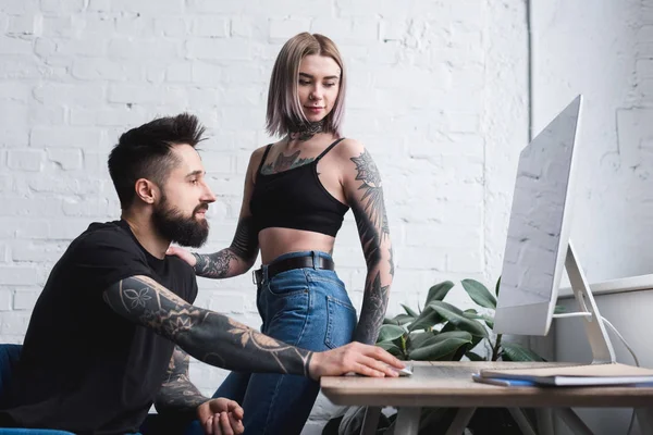 tattooed girlfriend looking at computer near boyfriend at home