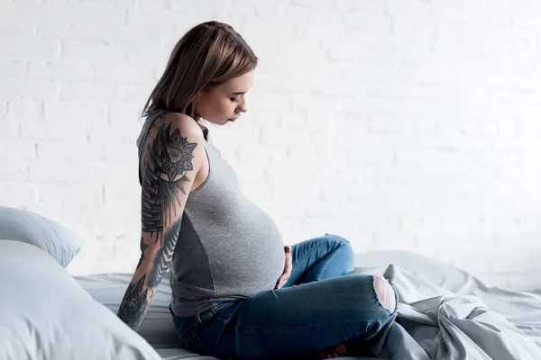 自宅のベッドの上に座って刺青妊婦の側面図 — ストック写真