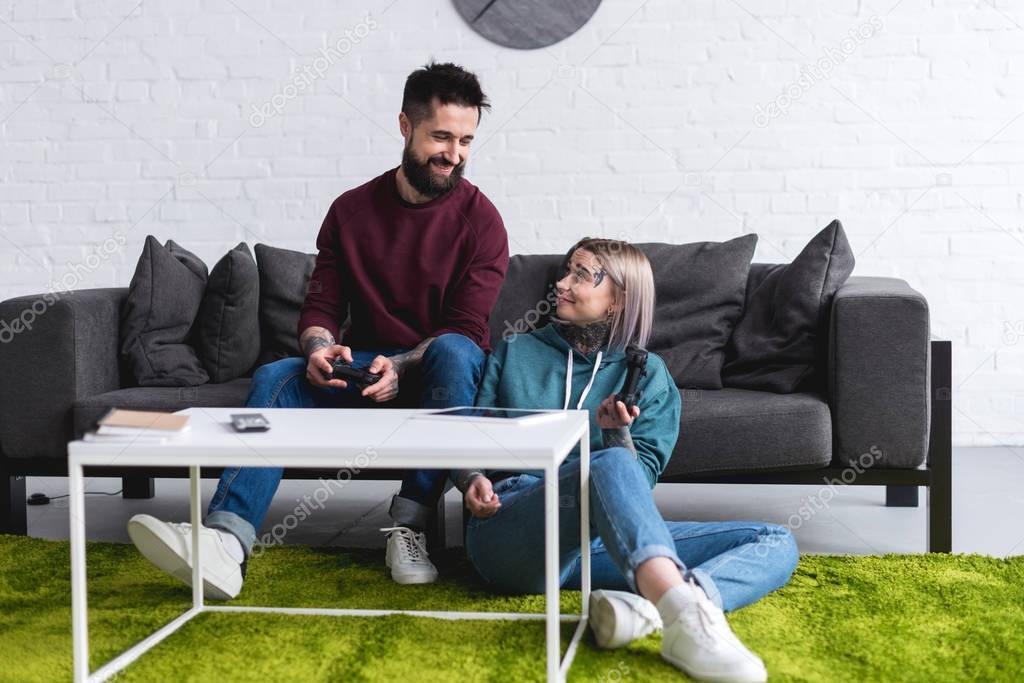 smiling tattooed couple playing video game and looking at each other