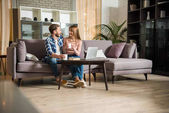 junges Paar sitzt auf Couch mit Tassen im Wohnzimmer mit modernem Design