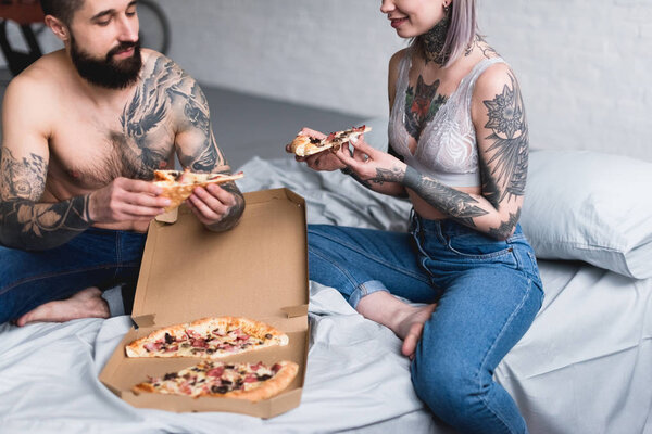 обрезанное изображение татуированной пары, поедающей пиццу дома
