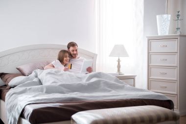 Yatakta yatan ve modern yatak odasında online alışveriş yaparken genç Çift