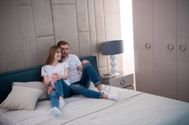 Yastıklar modern yatak odası ile yatak üzerinde oturan genç Çift