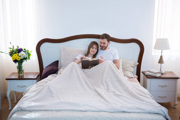 Front view of couple reading book in cozy modern bedroom