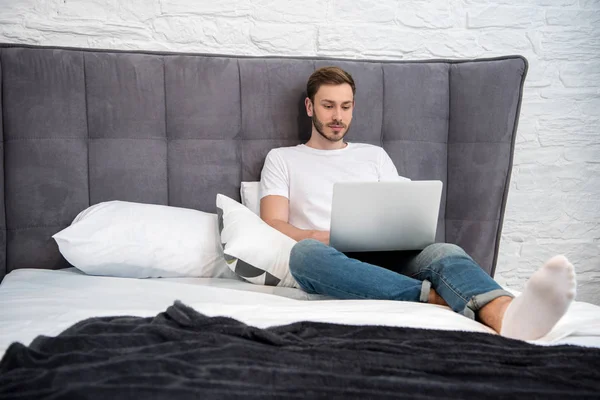 Front View Young Man Sitting Bed Using Laptop Modern Bedroom — Stock Photo, Image