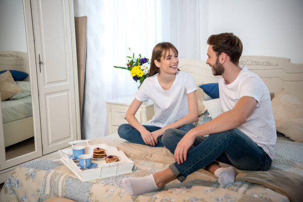 Couple on bed with breakfast on tray in cozy bedroom