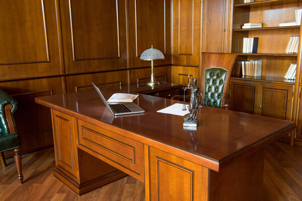 Interior of office room with laptop, statuette and papers on wooden table 
