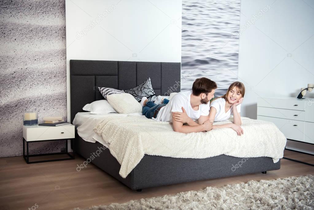 Smiling young couple lying in bedroom with design interior