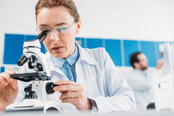 女性科学家的选择性聚焦在实验室中与同事在试剂上的仔细观察 — 图库照片